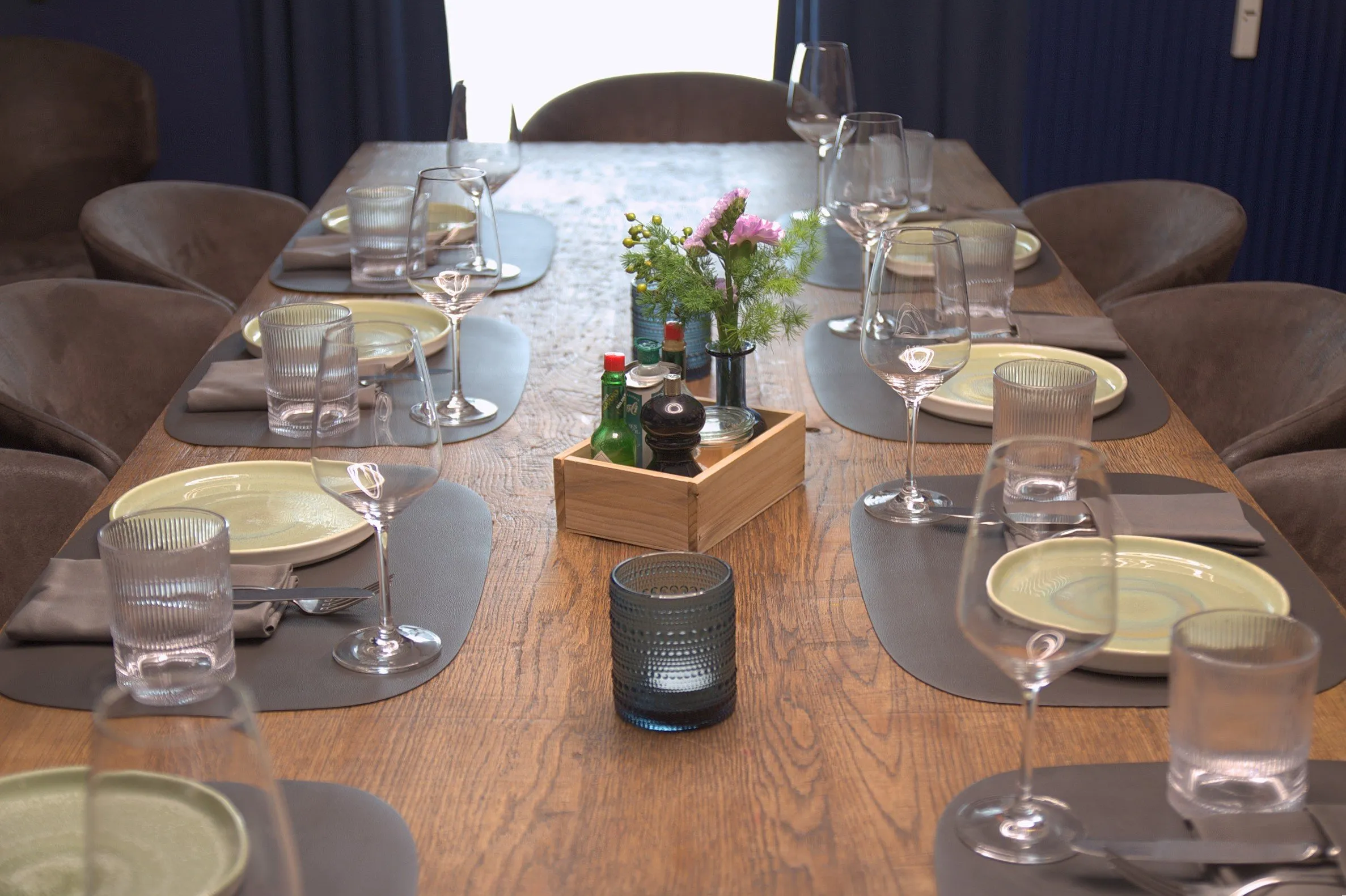Gedeckter Holztisch im Esszimmer mit Tellern, Gläsern und einem kleinen Blumenarrangement.
