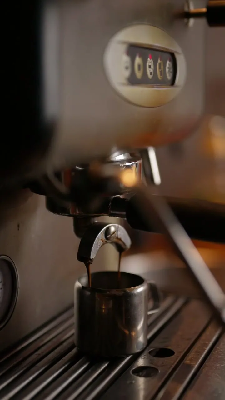 Standbild aus dem Espresso-Martini-Video: Espresso läuft aus dem Siebträger einer Espressomaschine in einen kleinen Edelstahlbecher.