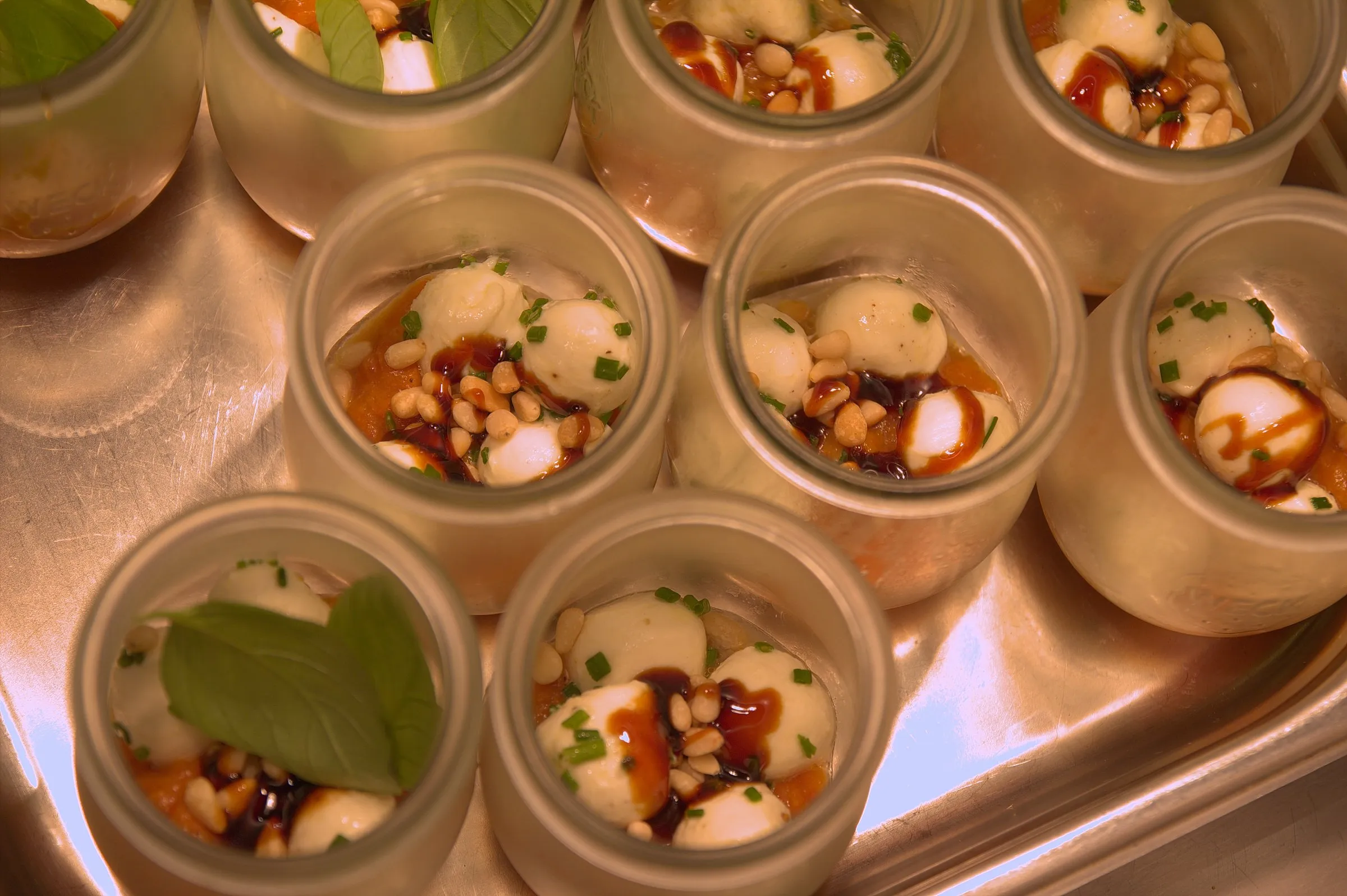 Gläser mit Mini-Mozzarella, Basilikum und Balsamico in einer Edelstahlwanne.