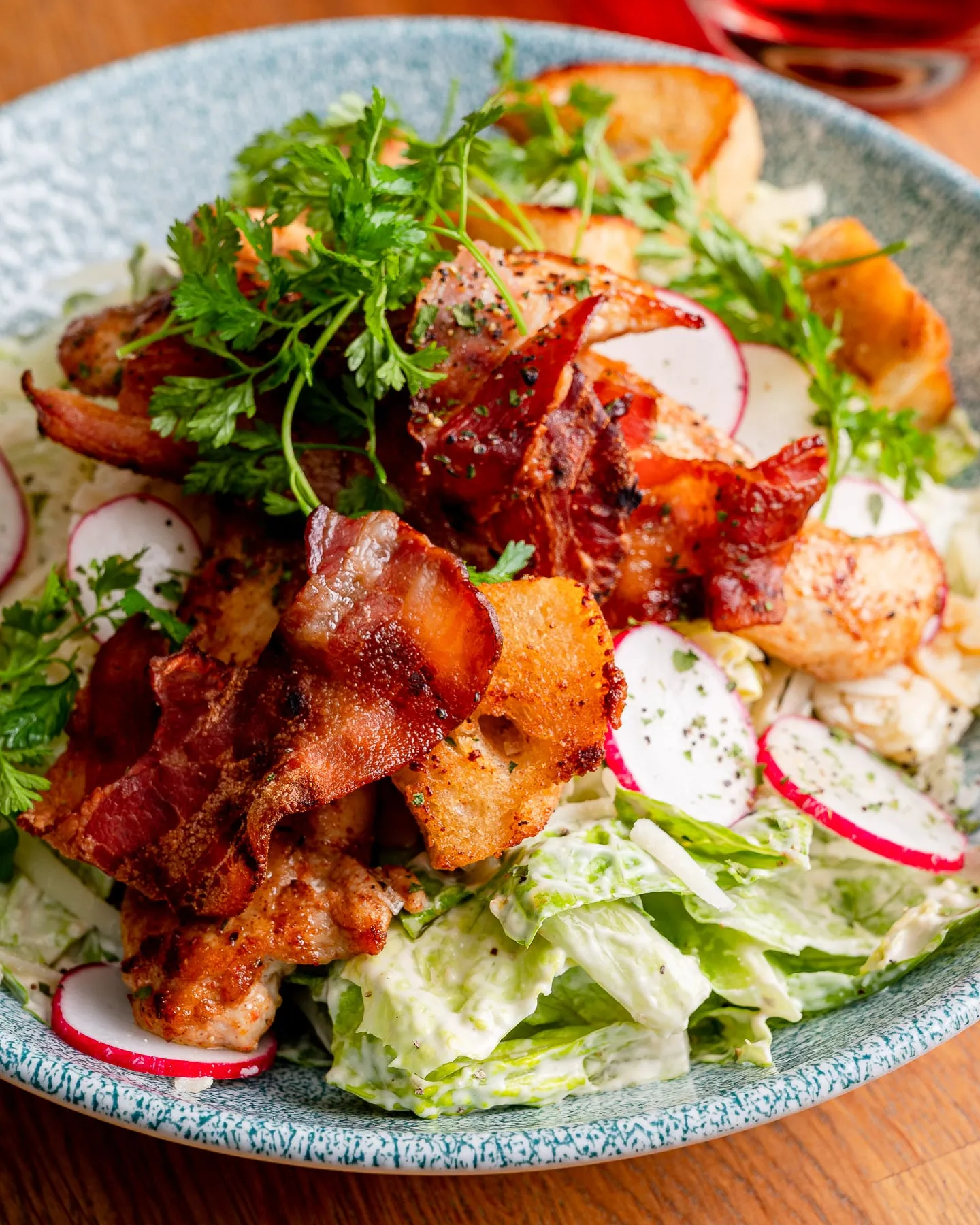 Salatschale mit knusprigem Bacon, gebratenem Hähnchen, Croutons, Radieschenscheiben und Kerbel auf cremigem Blattsalat.