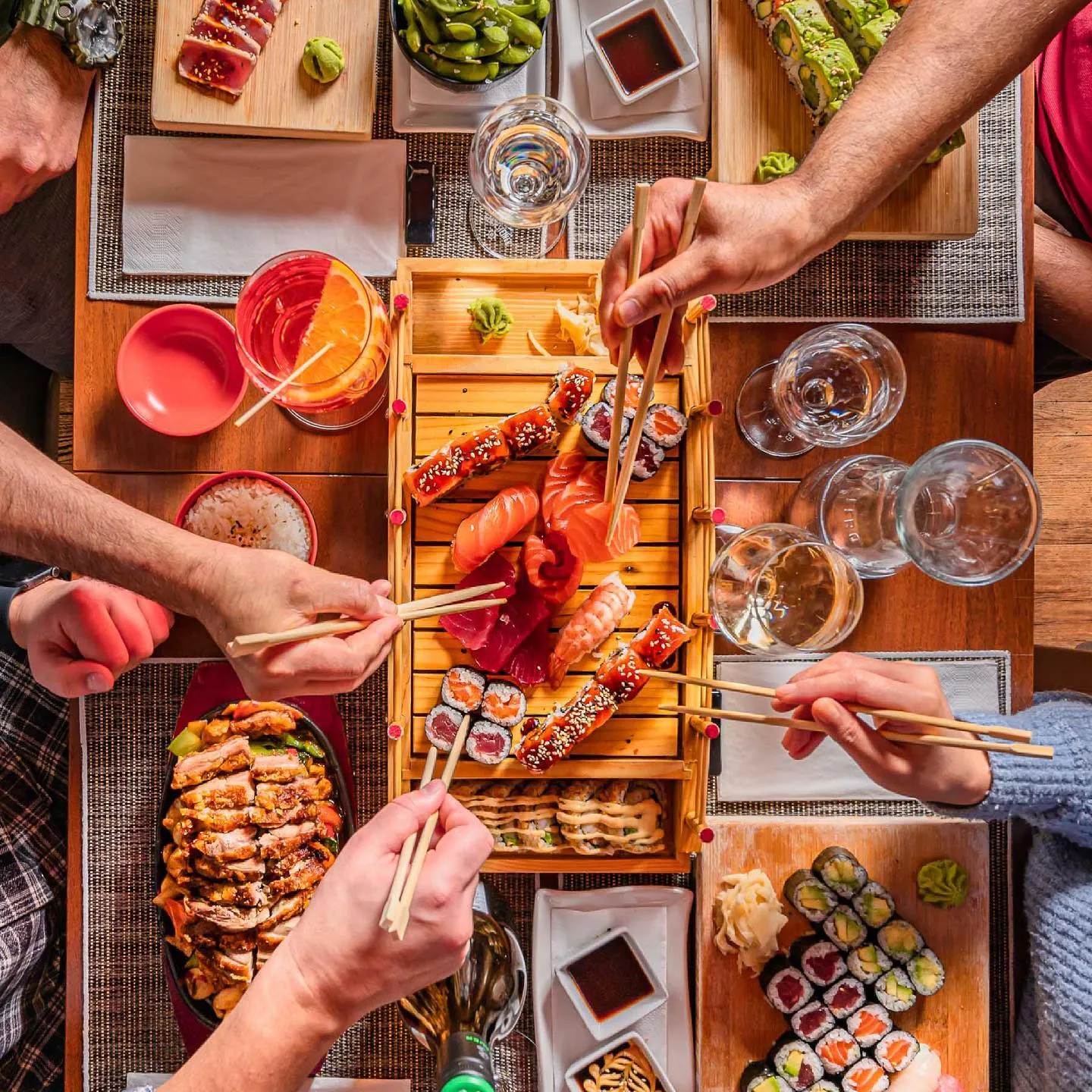 Gedeckter Tisch von oben, viele Hände greifen nach Sushi