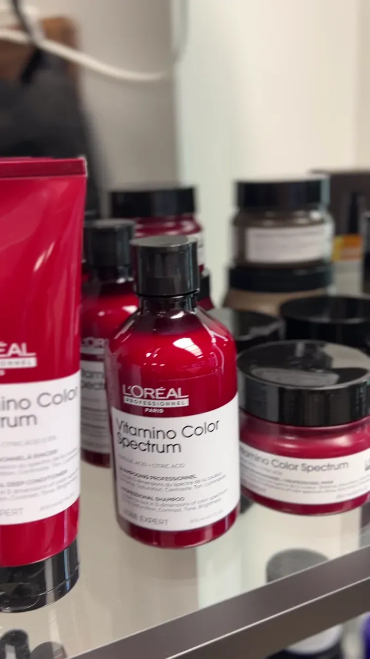 Das Produktregal im Salon: die pinkfarbene L’Oréal-Serie „Vitamino Color Spectrum“ mit Flaschen, Tuben und Masken auf einer Glasablage.