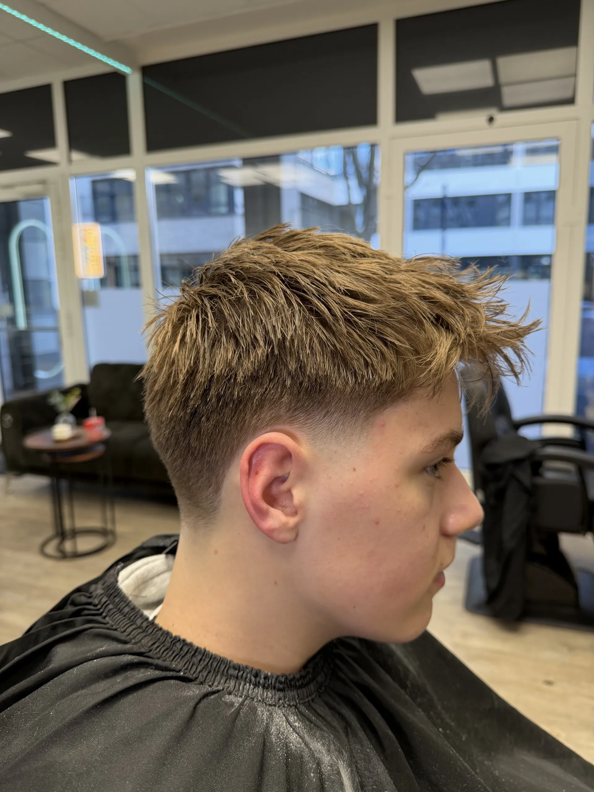 Herrenschnitt im Profil: blondes, texturiert nach oben gestyltes Deckhaar über mittlerem Fade.