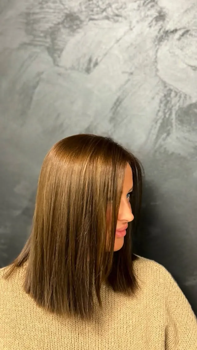 Brünetter Long Bob, stumpf auf Schulterhöhe geschnitten und glatt gestylt, im Profil vor einer grauen Spachtelwand.