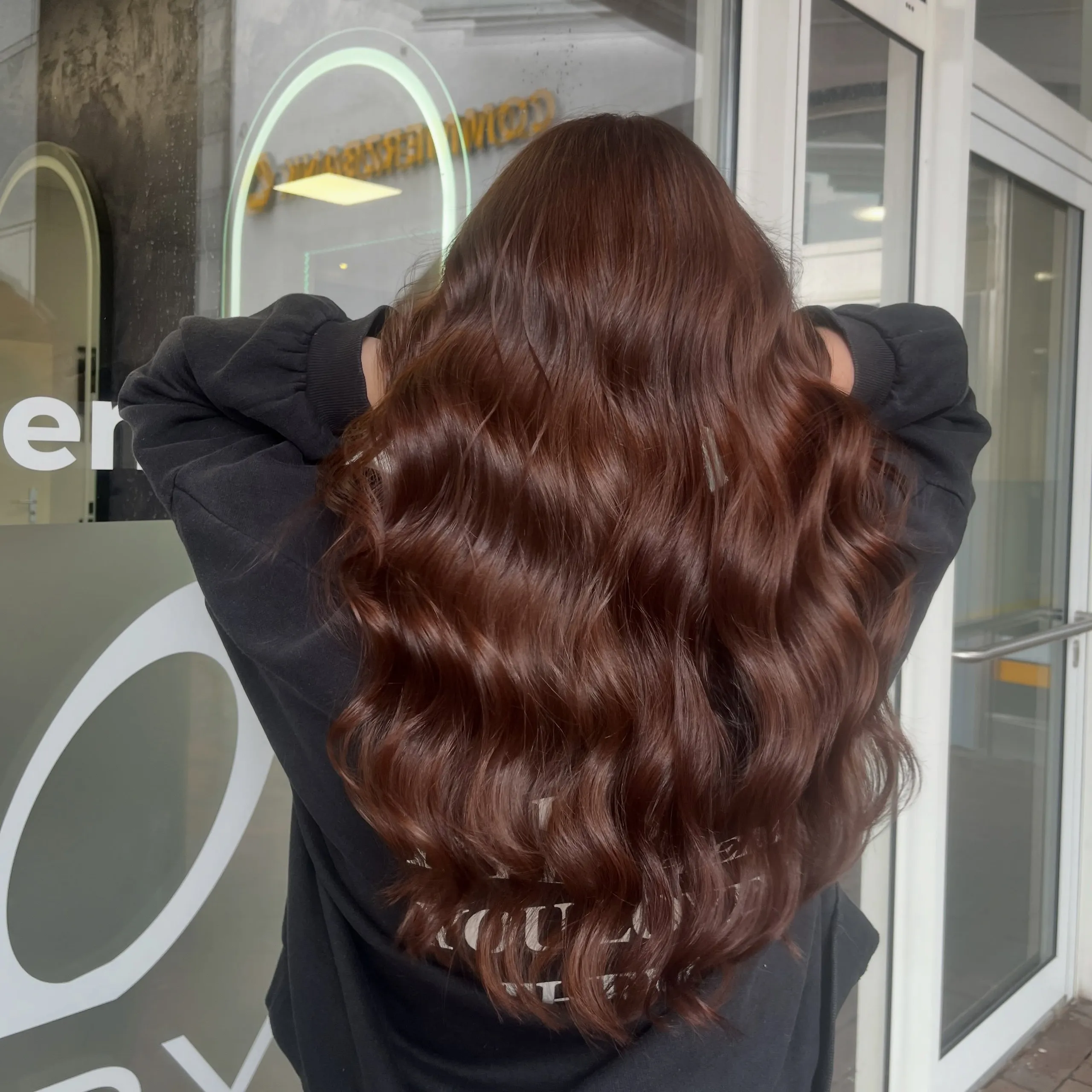 Lange, glänzende Wellen in rotbraunem Kastanienton, von hinten, die Hände im Haar.