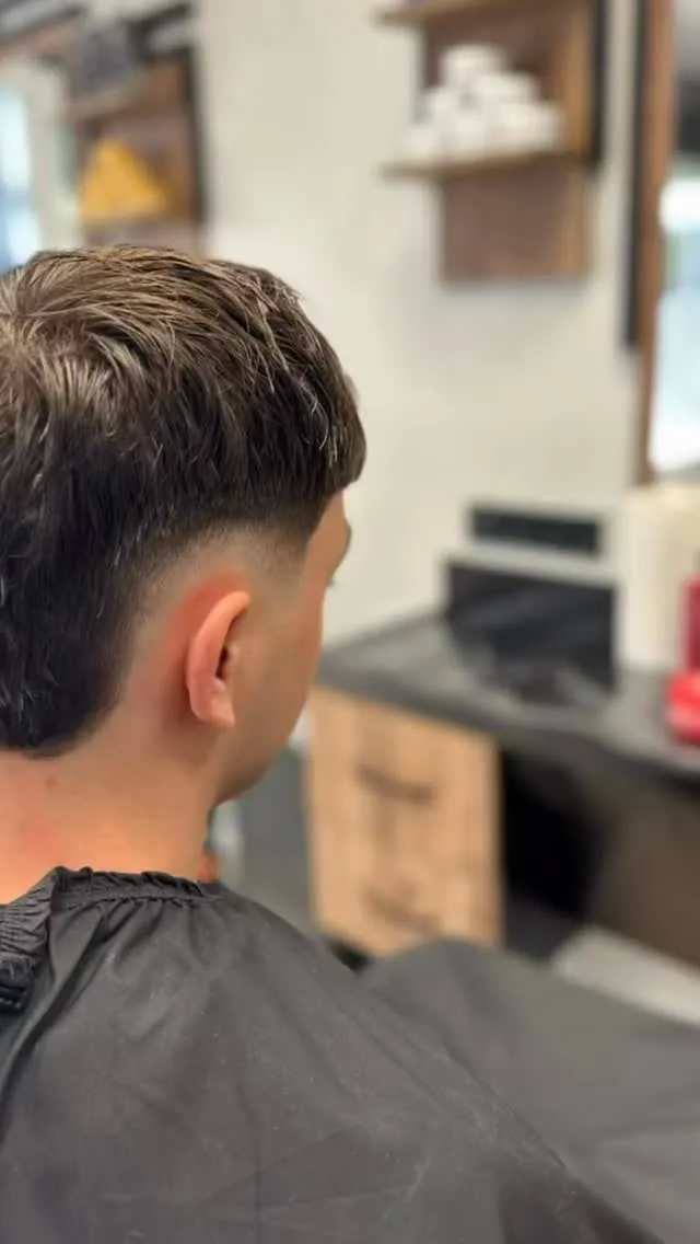 Herrenschnitt im Profil: welliges dunkles Deckhaar über einem tief angesetzten Fade an Seite und Nacken.