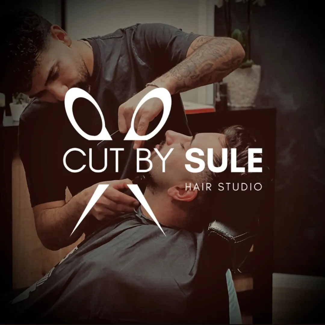 Marken-Kachel des Salons: Sule beim Bartschnitt, dunkel abgetönt, darüber großflächig das Logo CUT BY SULE mit den gekreuzten Scheren.