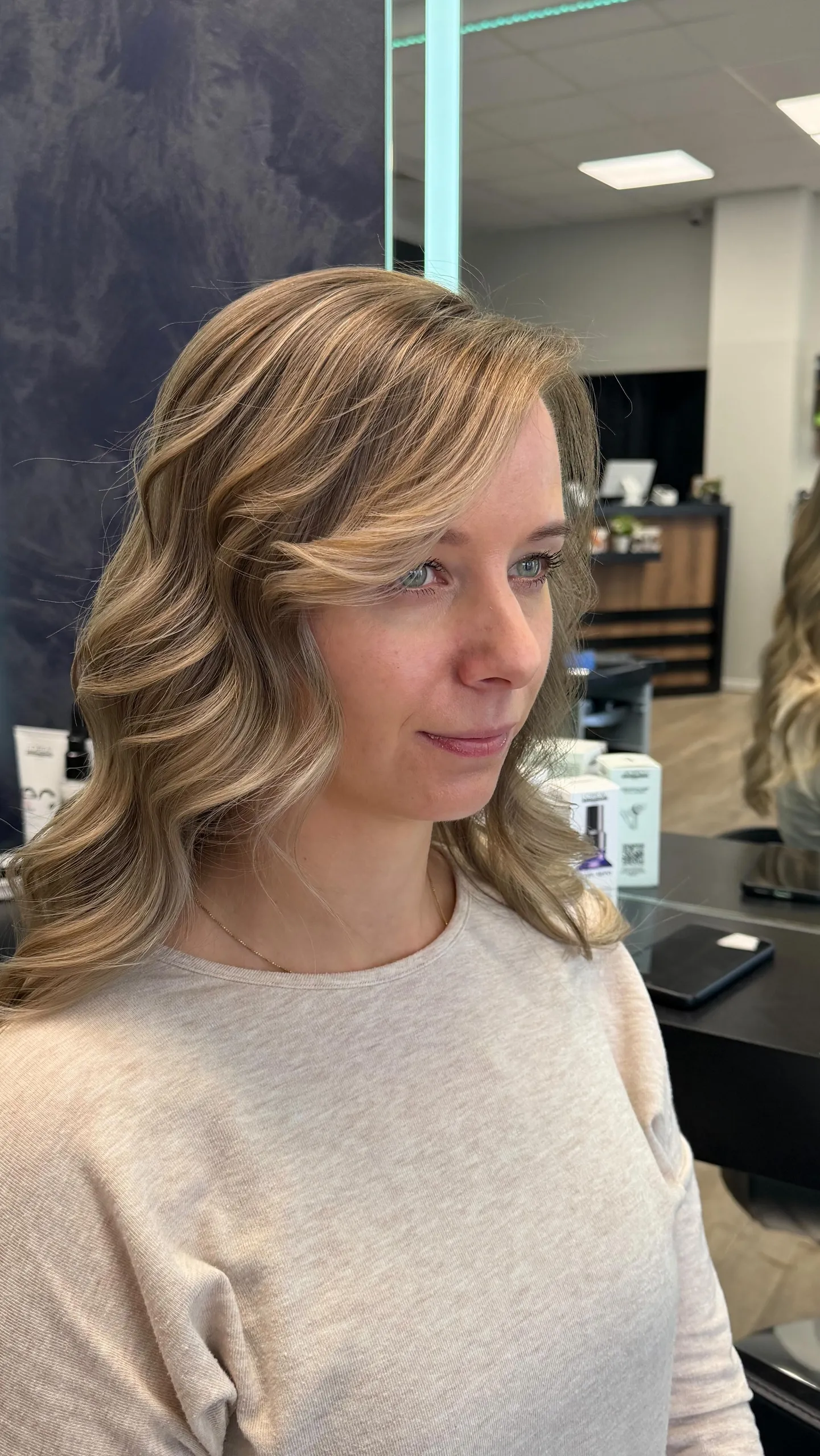Schulterlange Wellen in Blond mit hellen Gesichtssträhnen, seitlich im Salon fotografiert.