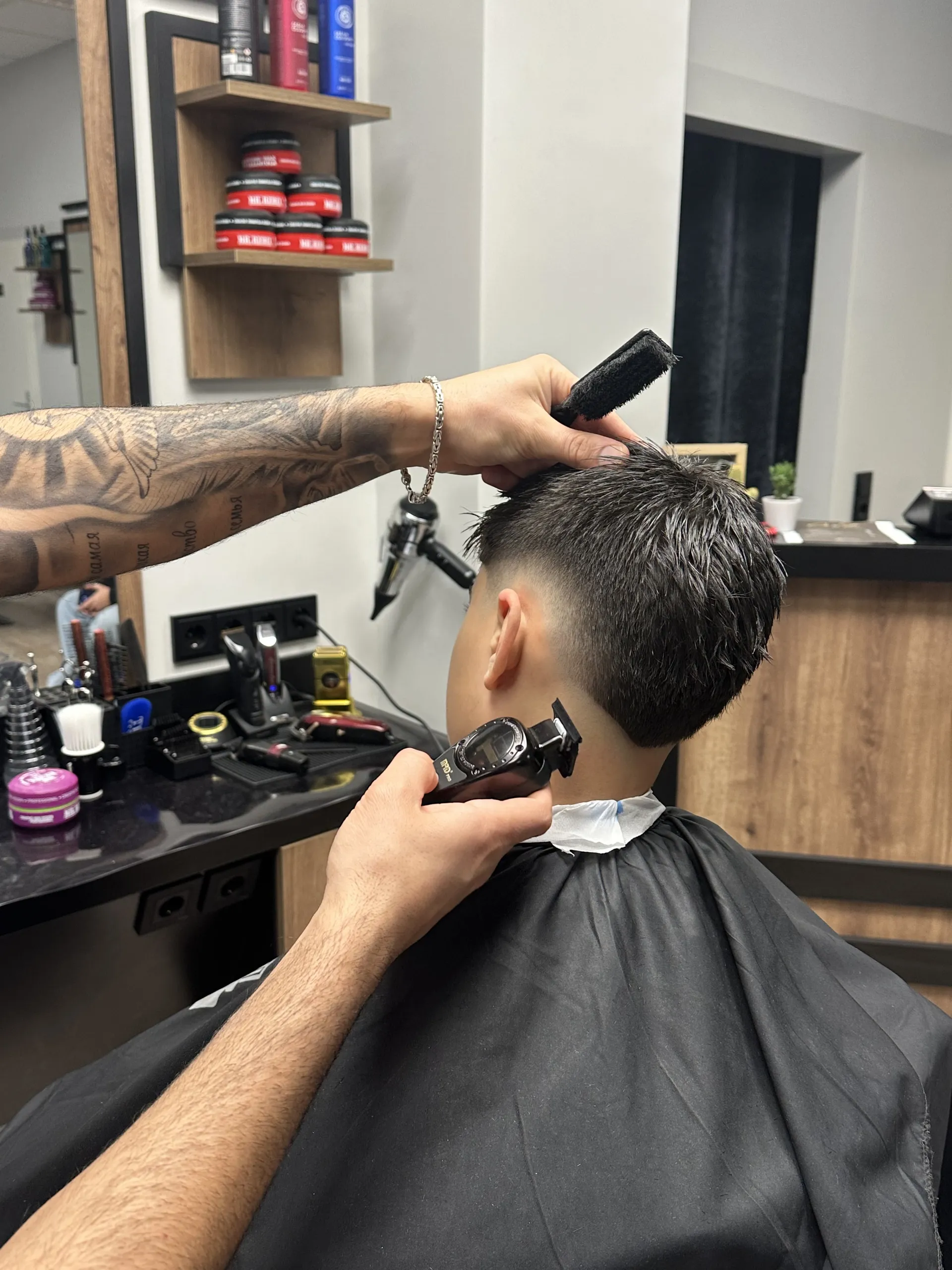 Arbeitsszene im Salon: die Nackenkontur wird mit dem Trimmer ausrasiert, dahinter das Produktregal.