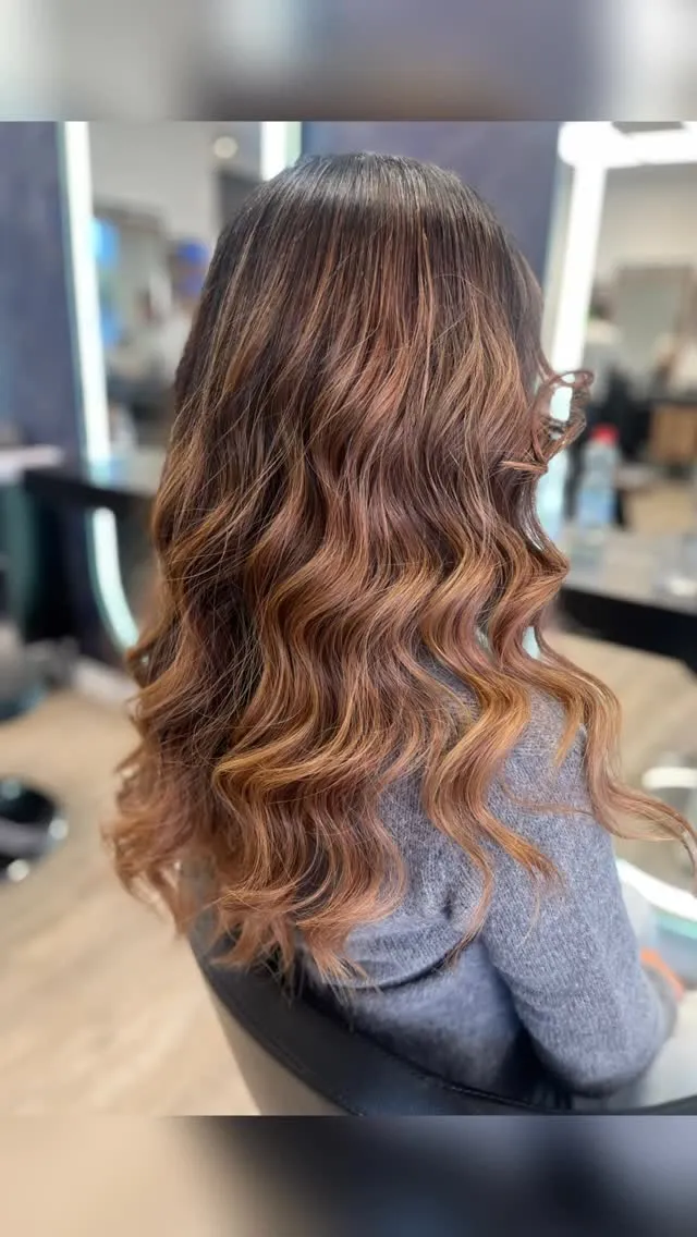 Lange Balayage von hinten: dunkler Ansatz, der in kupferfarbene Längen übergeht, in gleichmäßige Wellen gelegt.