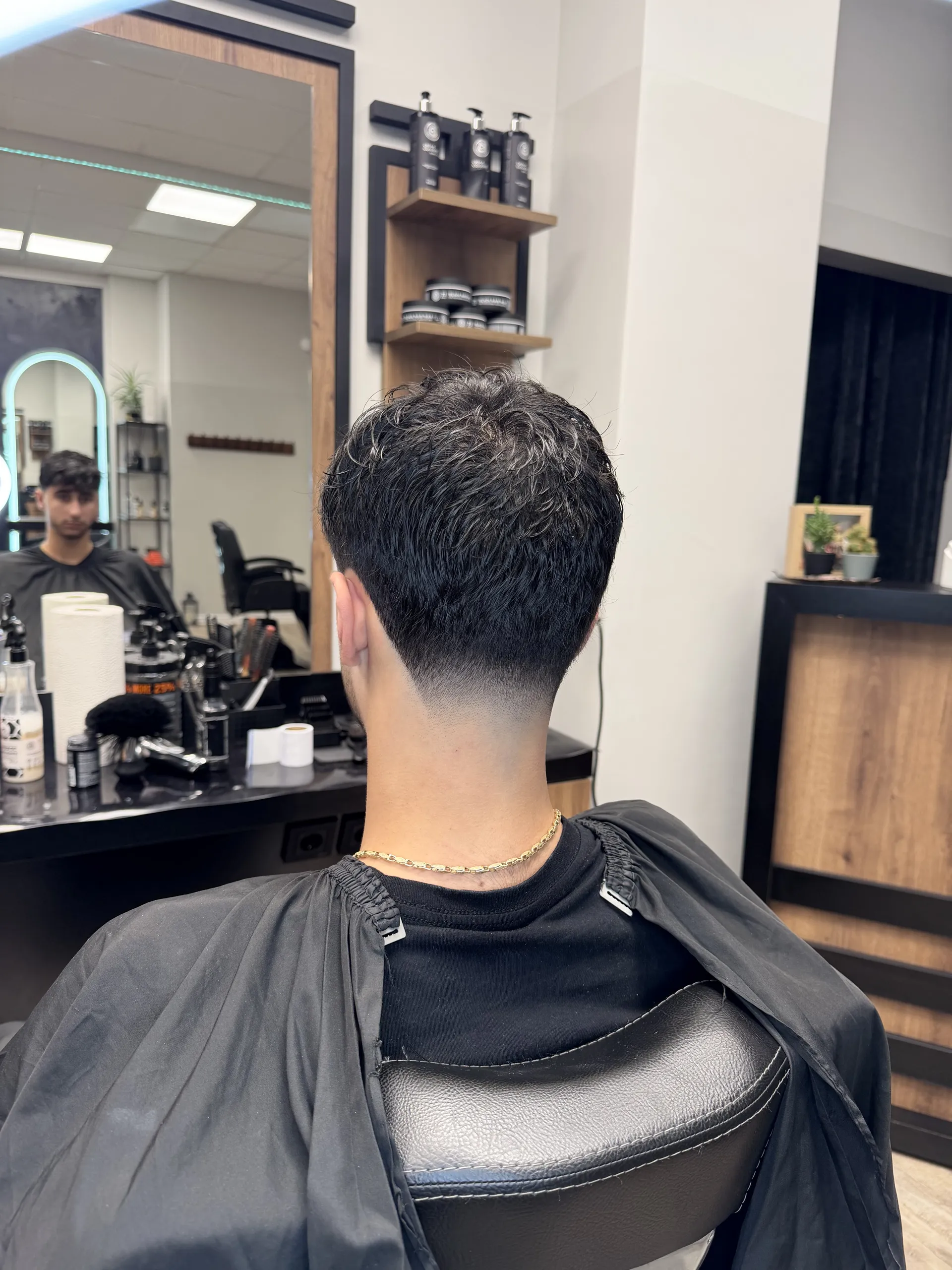 Herrenschnitt von hinten: kurzes, texturiertes dunkles Deckhaar über sauber ausrasiertem Nacken.