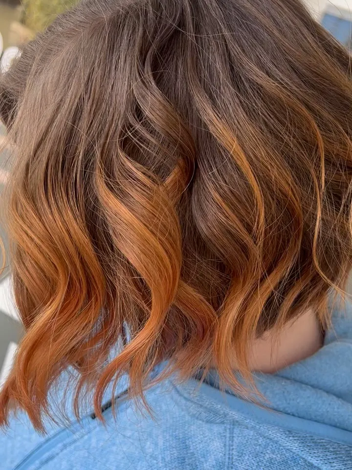 Gewellter Bob in Braun mit kupferfarbenen Balayage-Spitzen, von schräg hinten fotografiert.