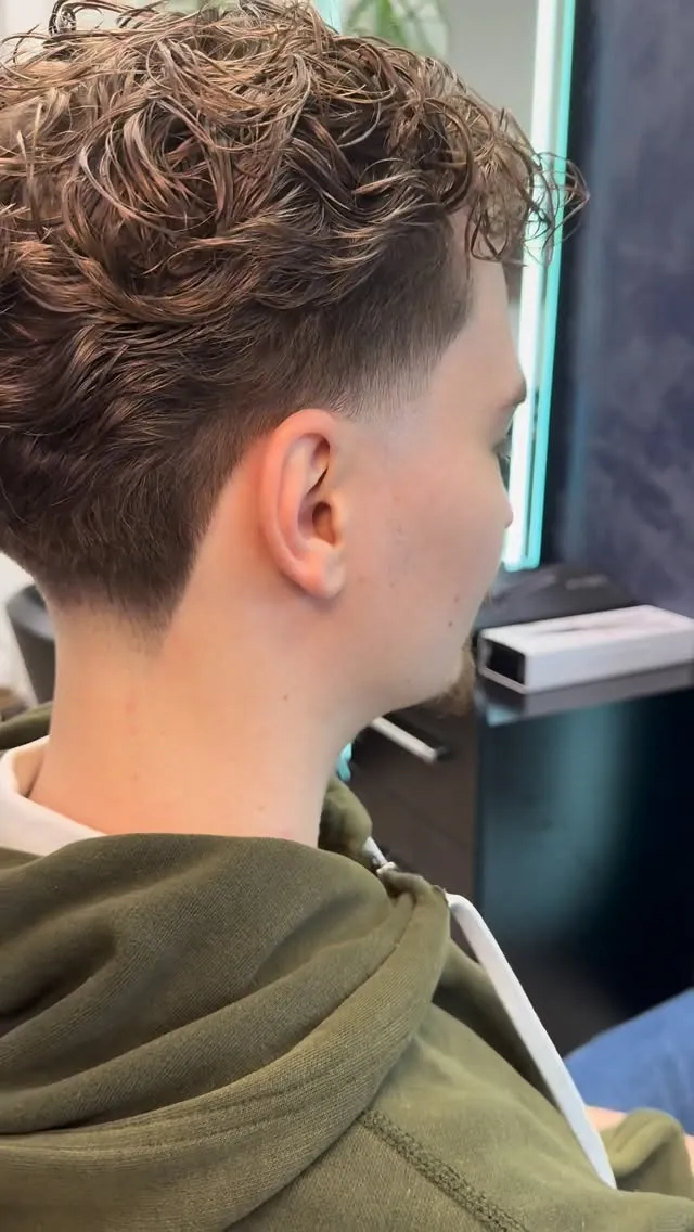 Herrenschnitt von hinten: lockiges braunes Deckhaar, an Seiten und Nacken zu einem weichen Taper ausrasiert.
