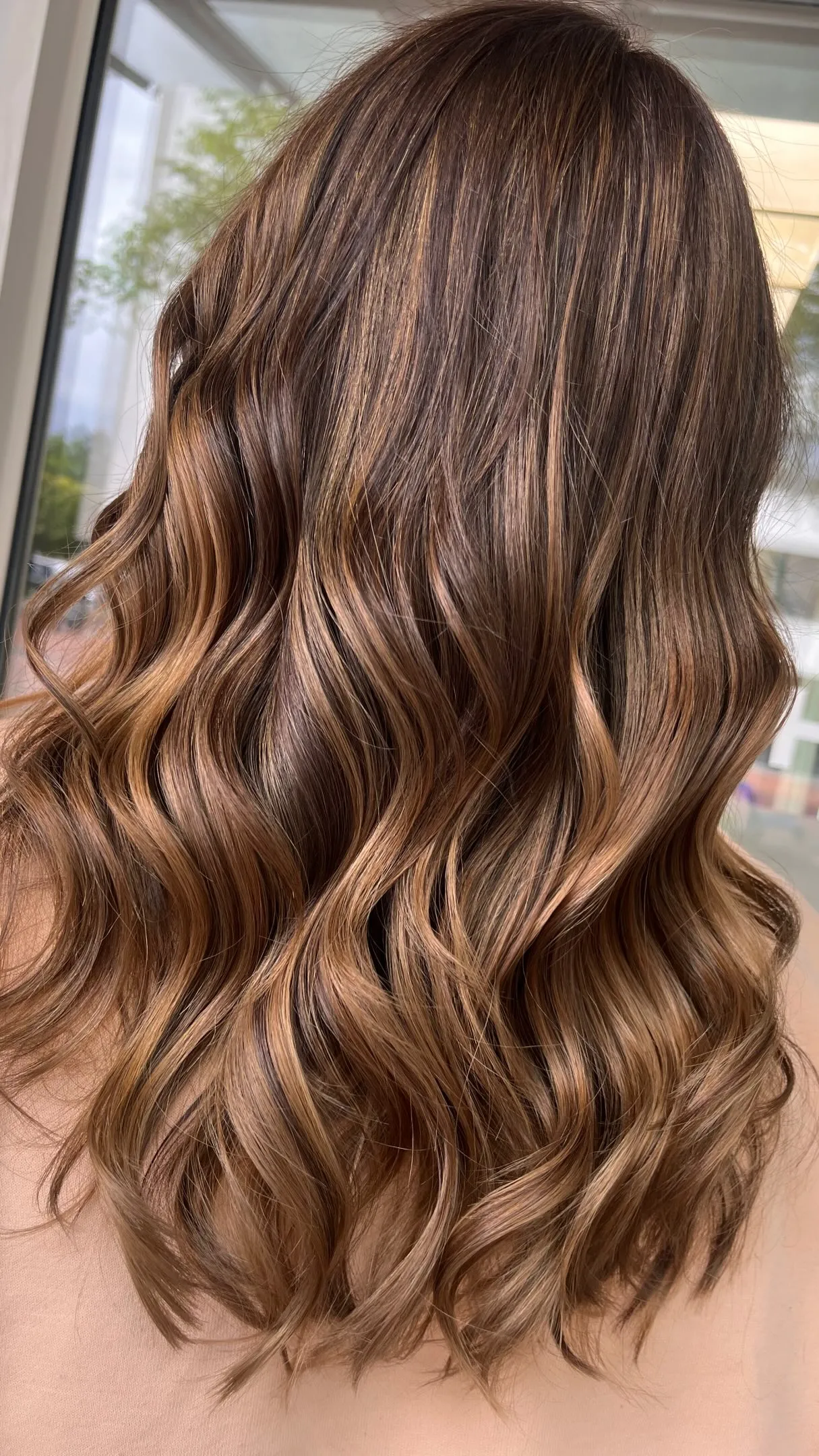 Lange, voluminöse Wellen in Karamellbraun mit honigfarbener Balayage, von hinten fotografiert.