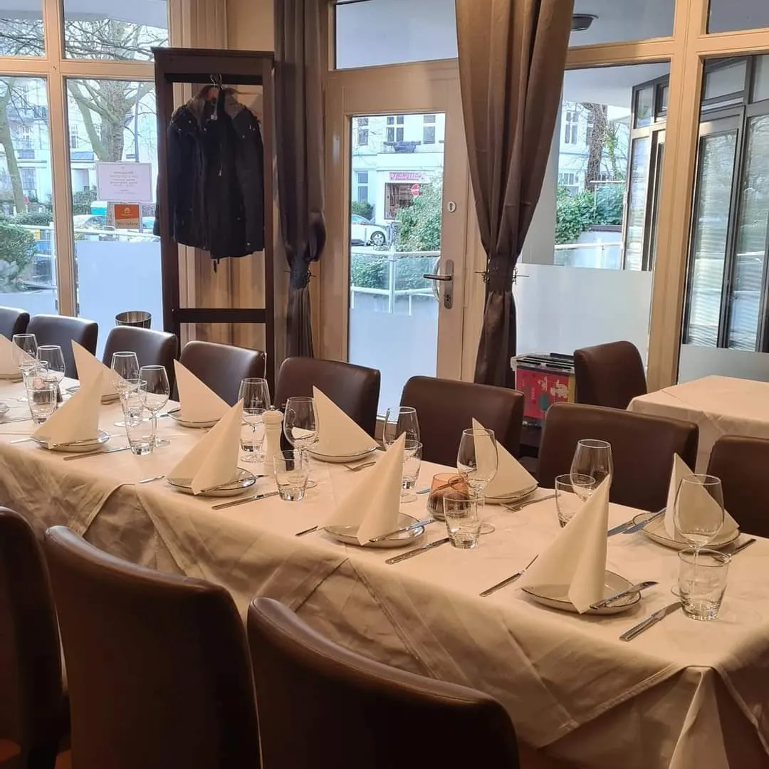 Festlich eingedeckte Tafel mit beigen Tischdecken und gefalteten Servietten, im Hintergrund die Garderobe.