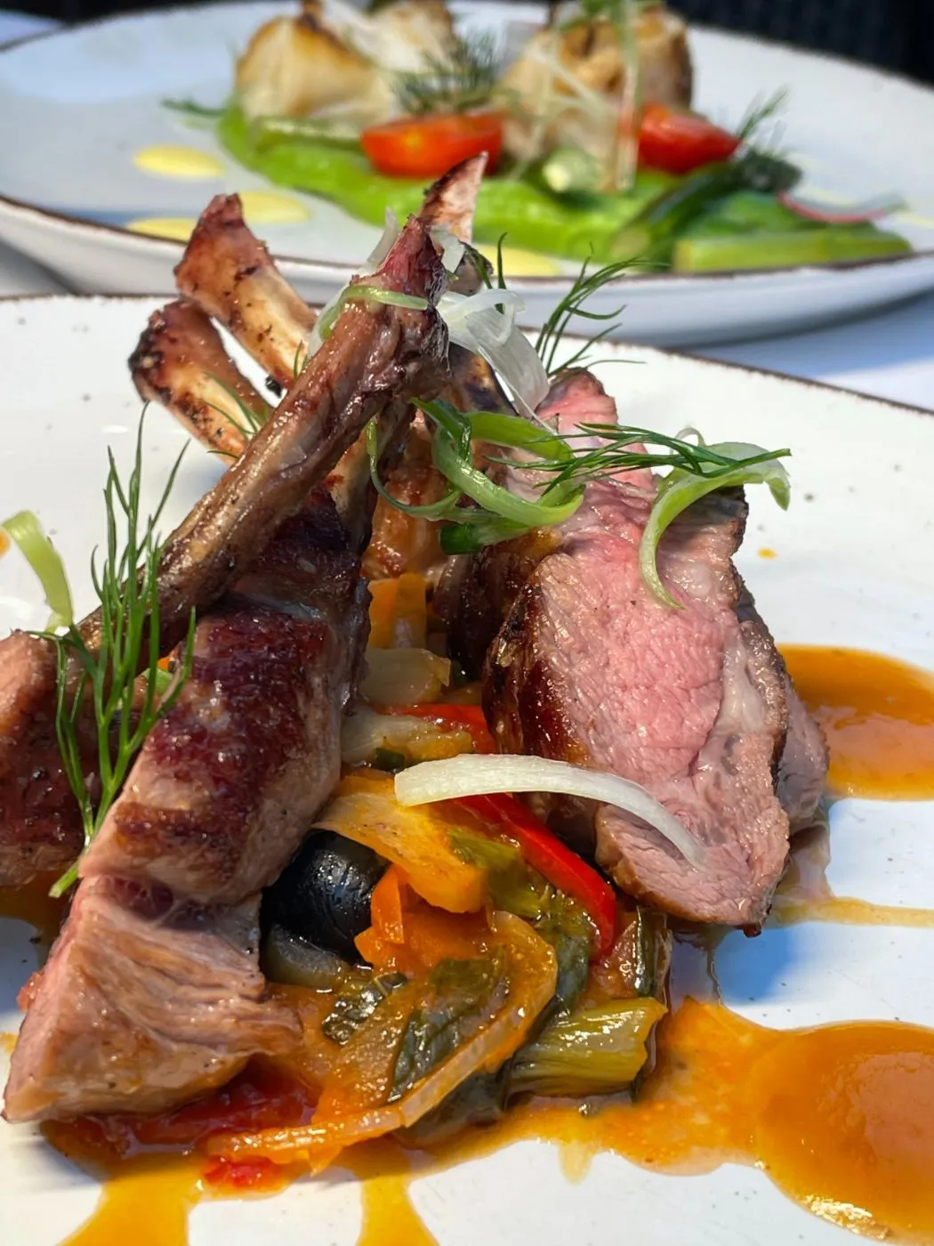 Rosa gebratenes Lammkarree mit Kräutern, Gemüse und orangefarbener Sauce, schräg von vorn fotografiert.