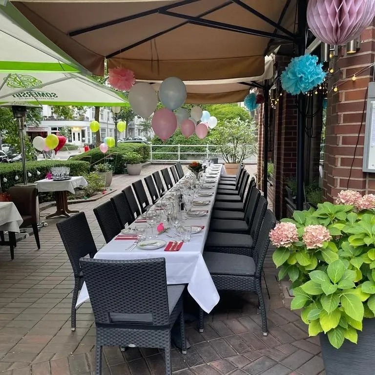 Terrasse mit festlich gedeckter Tafel, Papierblumen-Deko und Hortensien, im Hintergrund Bäume.