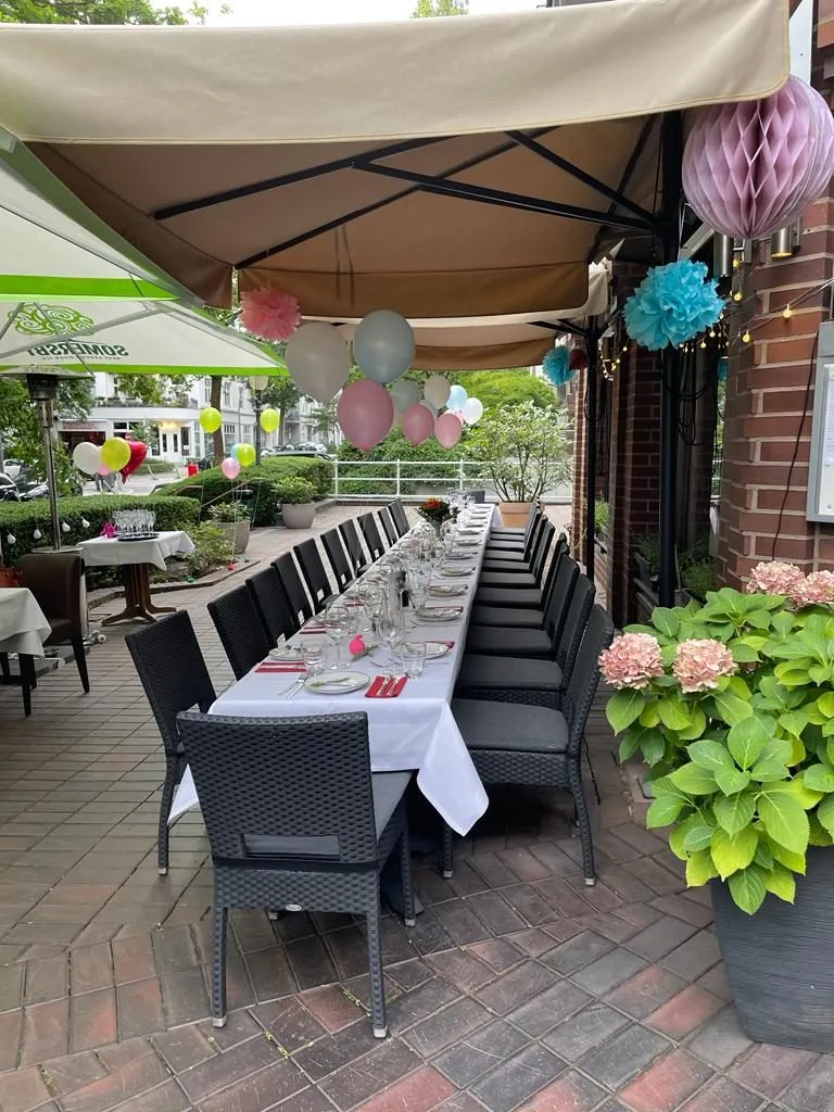 Überdachte Terrasse mit einer langen, weiß gedeckten Tafel, Rattanstühlen, Hortensien und bunten Ballons.