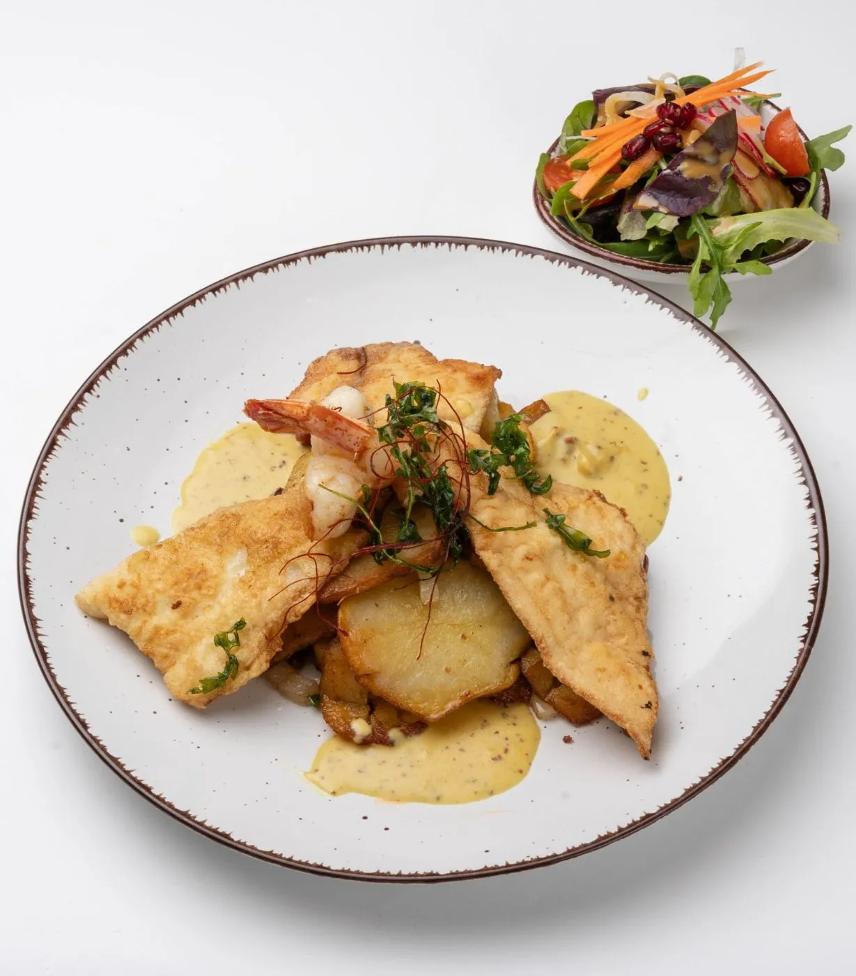 Hamburger Pannfisch: Fischfilet mit Garnelen auf Bratkartoffeln und Senfsauce, daneben eine kleine Salatschale.