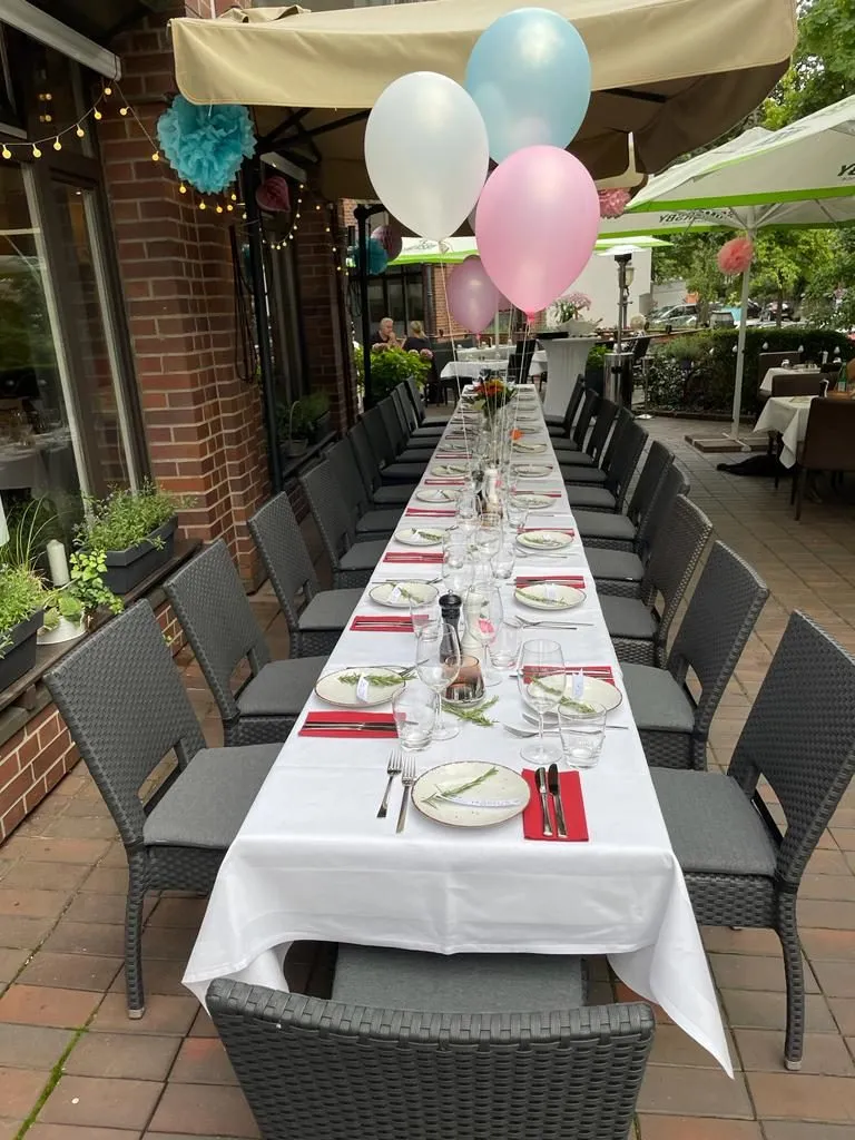 Für eine Feier gedeckte lange Tafel auf der Terrasse mit Luftballons unter der Markise.