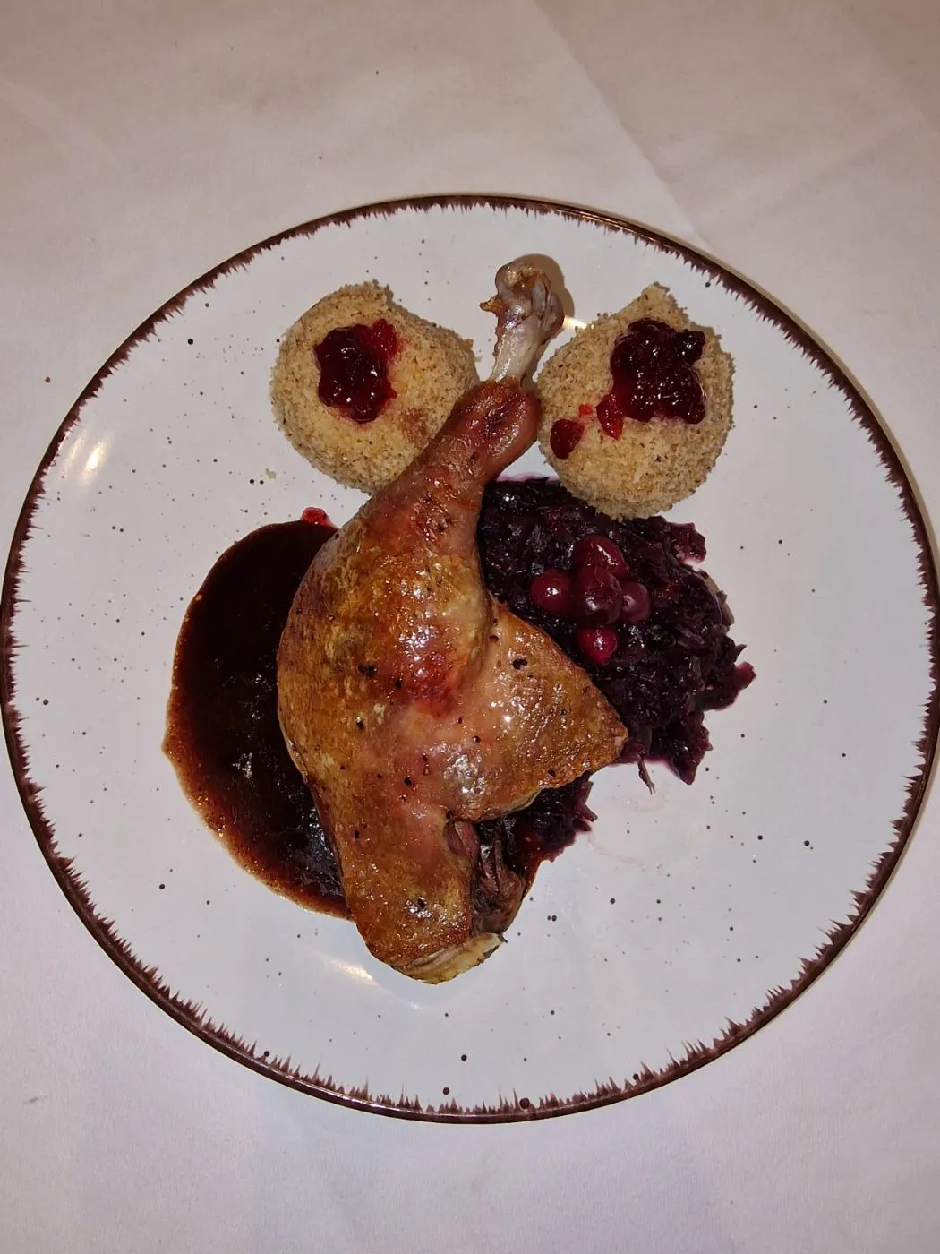 Knusprige Entenkeule mit dunkler Sauce, Rotkohl und zwei Knödeln mit Preiselbeeren, von oben fotografiert.